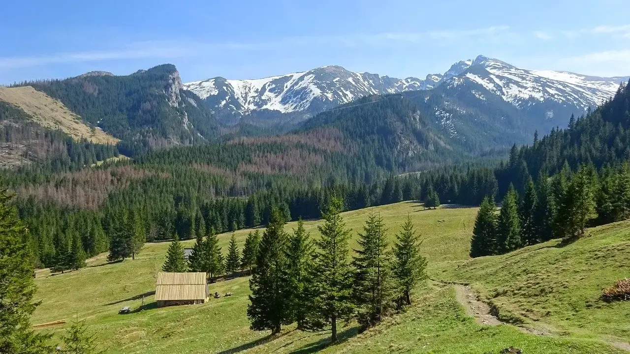 Piękne trasy Tatry. Zielone hale, lasy i ośnieżone szczyty. Drewniana chata i ścieżka zapraszają do wędrówki.