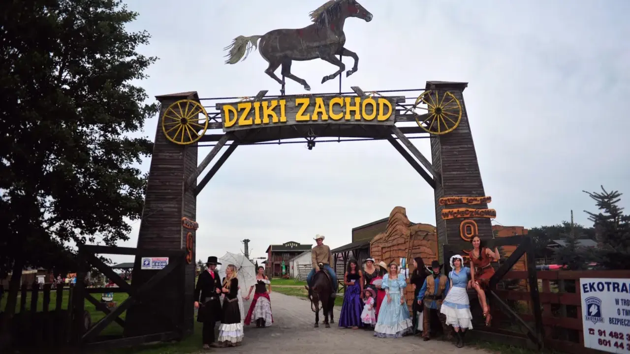 Park rozrywki Dziki Zachód koło Kołobrzegu. Grupa osób w strojach z Dzikiego Zachodu pozuje przed bramą.
