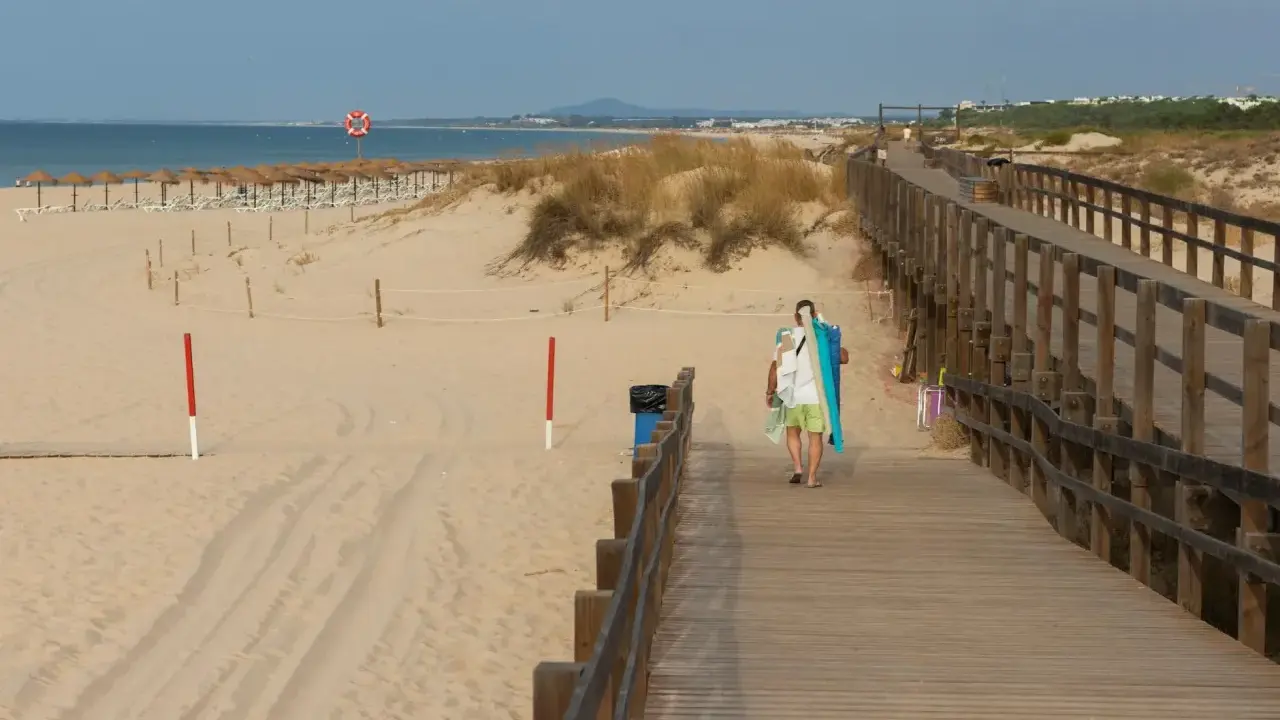 Spacer plaży z drewnianą kładką i osobą niosącą sprzęt plażowy. Grzybowo atrakcje czekają!