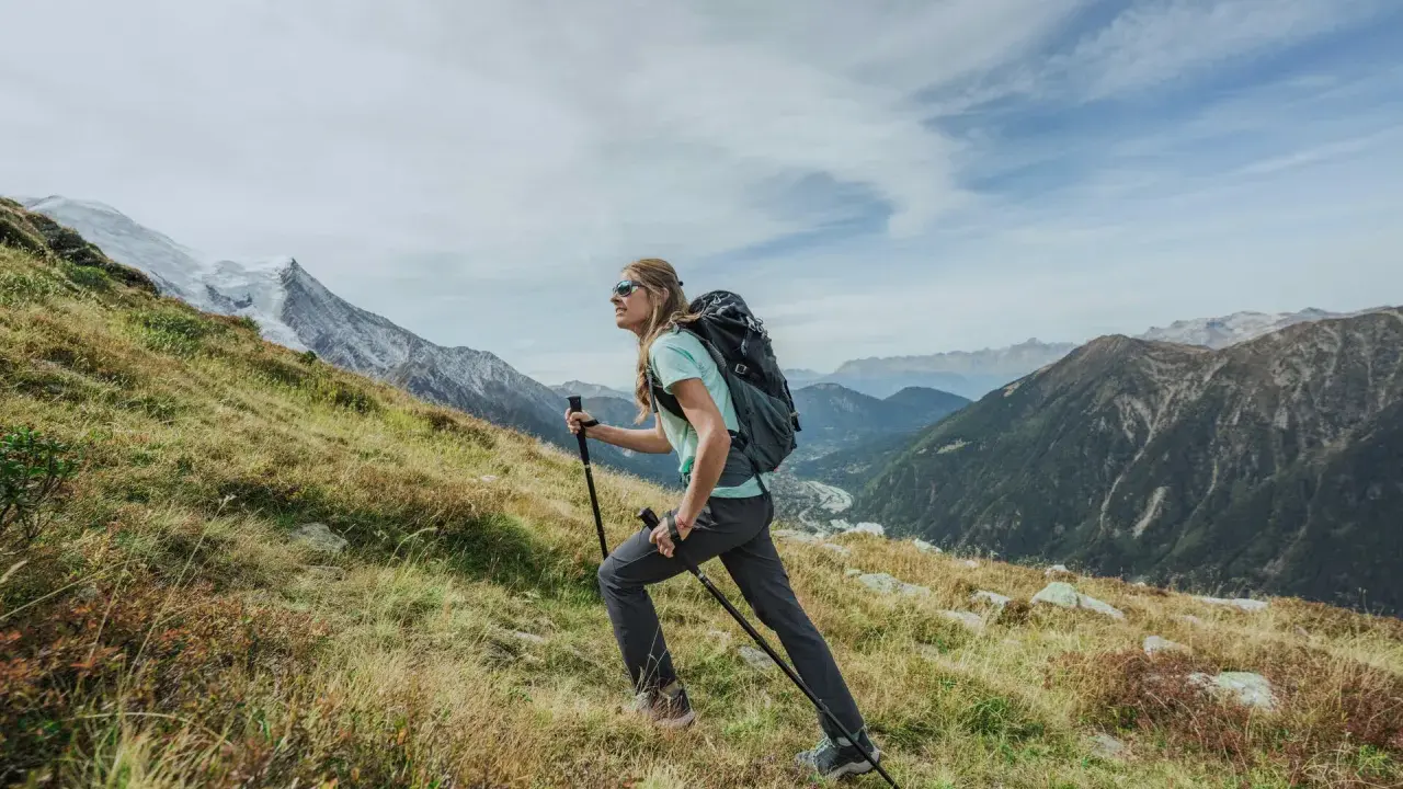 Kobieta z plecakiem i kijkami wspina się po zboczu. Widok gór i doliny. Zastanawia się, ile się idzie na Giewont.