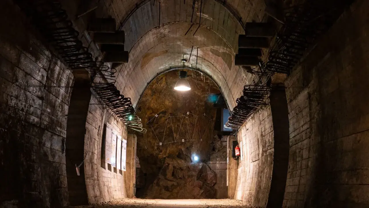 Wnętrze tunelu w Górach Sowich. Betonowe ściany, łukowe sklepienie i oświetlenie tworzą mroczny klimat.
