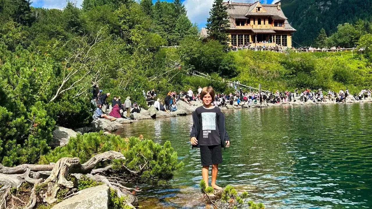 Chłopiec stoi nad jeziorem, a w tle widać ludzi i górski pensjonat. To świetne atrakcje w górach dla dzieci.