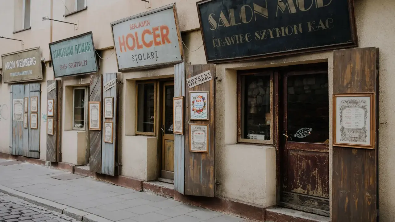 Urokliwe szyldy sklepów w Kazimierzu w Krakowie: "Salon Mód", "Holcer Stolorz", "Stanisław Nowak Sklep Spożywczy" i inne.