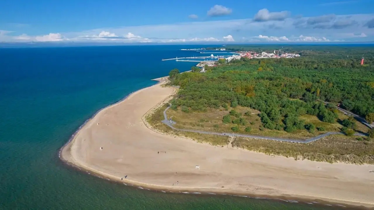 Piękna plaża i las na Helu. W oddali widać miasteczko i port, idealne miejsce na wakacyjne atrakcje.