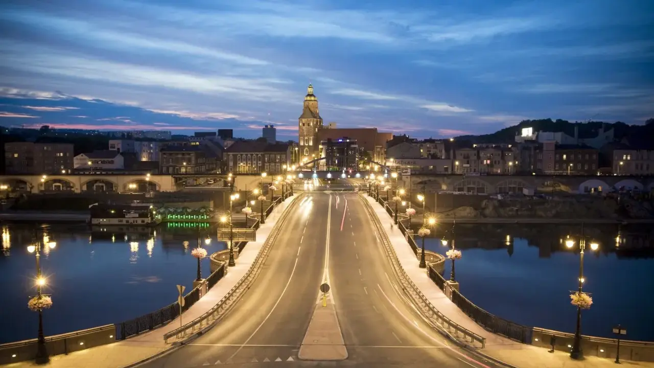Most w Gorzowie Wielkopolskim nocą, oświetlony latarniami, z widokiem na miasto i wieżę kościelną. Atrakcje miasta w wieczornym blasku.