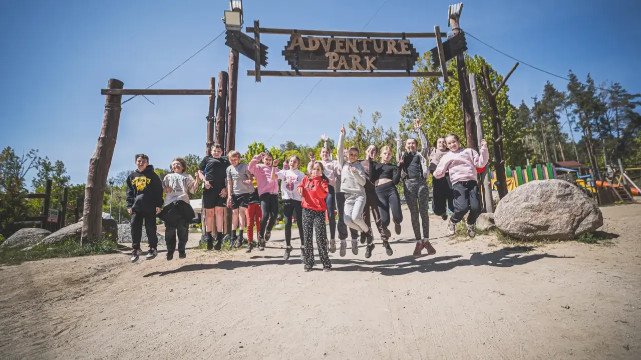 Radosna grupa dzieci skacze przed bramą "Adventure Park" w Gdyni.