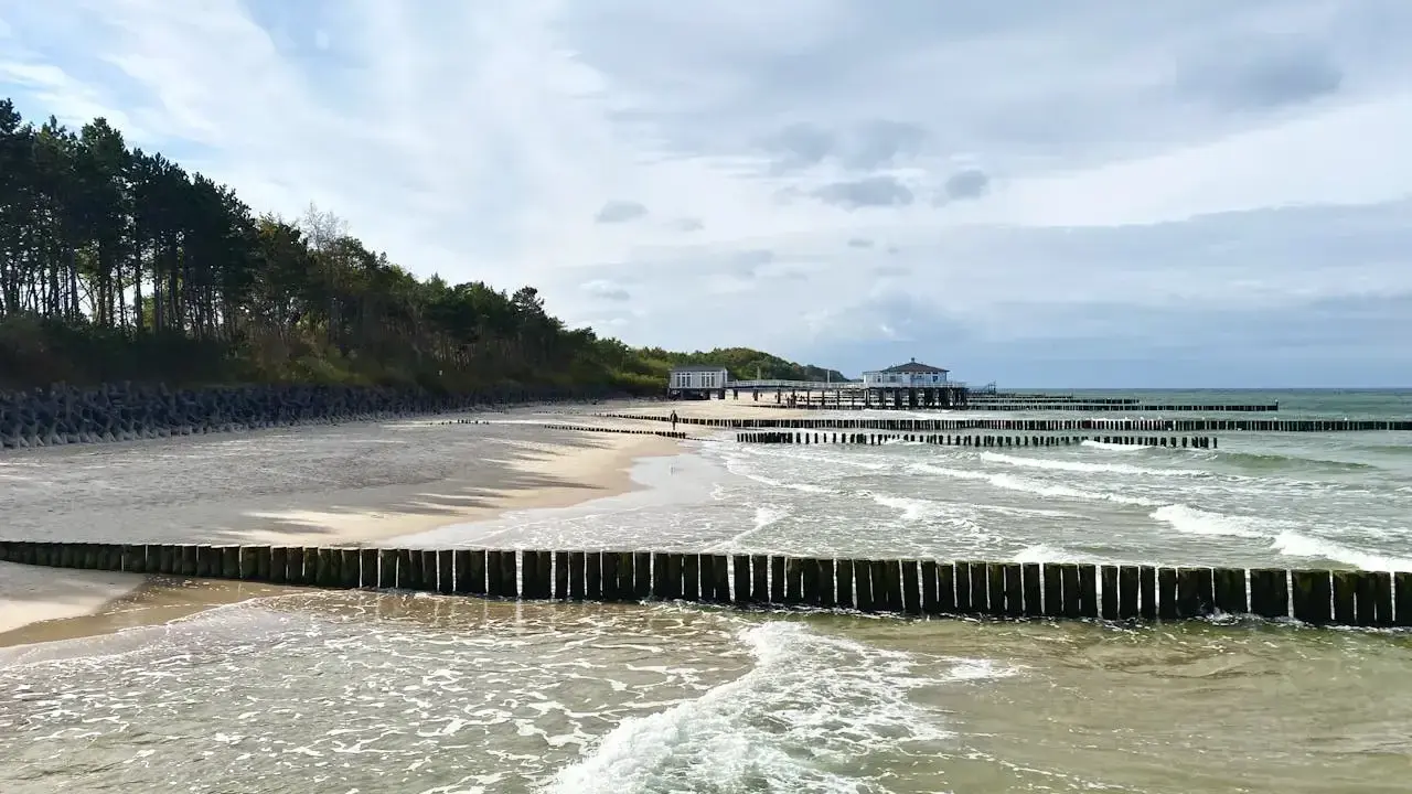 Plaża z drewnianymi falochronami i budynkami nad morzem, przypominająca najcieplejsze regiony Polski.