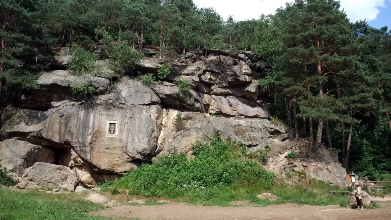 Skalny krajobraz w Polsce, z imponującymi formacjami skalnymi porośniętymi lasem sosnowym. Na skale widoczna tablica pamiątkowa.