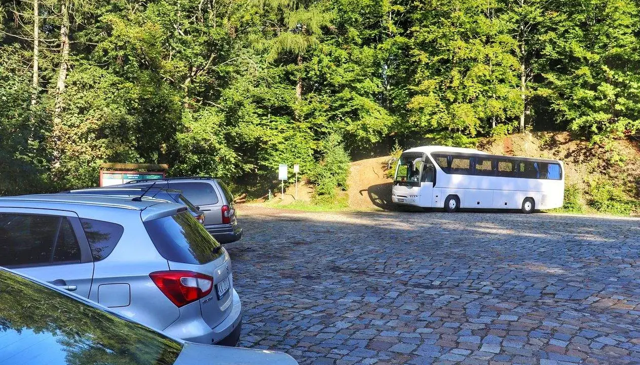 Parking na czupel trasie. Biały autokar i samochody na brukowanym placu wśród zieleni.
