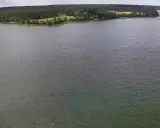 Rozległe jezioro Wdzydze otoczone lasem i zielonymi polami. Spokojna tafla wody odbija niebo.