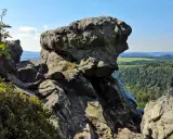 Wielkie, szare skały górują nad zieloną doliną. W oddali widać białe skały i pagórki.