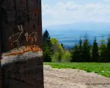 Rdzawy słup z rysunkami jeleni na tle górskich szlaków i lasów. Widok z Turbacza.