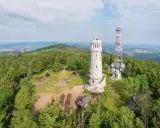 Wieża widokowa i maszt telekomunikacyjny na szczycie porośniętym lasem. W oddali rozciągają się góry Sowie, a wokół widać liczne szlaki turystyczne.