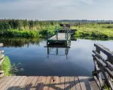 Drewniana kładka i prom na spokojnej wodzie. Biebrzański Park Narodowy atrakcje przyrodnicze zachwycają.