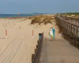 Spacer plaży z drewnianą kładką i osobą niosącą sprzęt plażowy. Grzybowo atrakcje czekają!