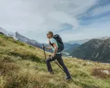 Kobieta z plecakiem i kijkami wspina się po zboczu. Widok gór i doliny. Zastanawia się, ile się idzie na Giewont.