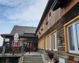 Drewniane schronisko w Górach Opawskich, z tarasem i schodami. W tle błękitne niebo z chmurami.