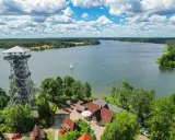 Wieża widokowa i zabudowania nad jeziorem, idealne miejsce na odkrywanie **Gowidlino atrakcje**. Żaglówka na wodzie.