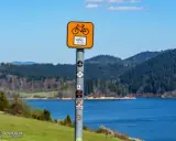 Znak Velo Dunajec zapowiada piękną trasę rowerową. Jezioro i góry tworzą malowniczy krajobraz.