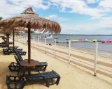 Plaża nad Jeziorem Nyskim z leżakami i parasolami. W tle widać wodę, pomost z łódkami i statek wycieczkowy. Idealne miejsce na wypoczynek i odkrywanie atrakcji.