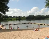 Słoneczna mazury plaża z ludźmi odpoczywającymi na piasku i kąpiącymi się w jeziorze. Drewniane molo w wodzie.