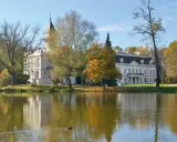 Pałac w Bolimowskim Parku Krajobrazowym odbija się w spokojnej tafli jeziora, otoczony jesiennymi drzewami.