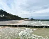 Plaża z drewnianymi falochronami i budynkami nad morzem, przypominająca najcieplejsze regiony Polski.