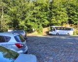 Parking na czupel trasie. Biały autokar i samochody na brukowanym placu wśród zieleni.