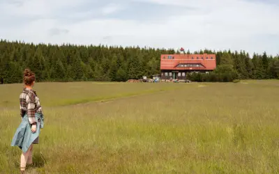 Dziewczyna w kratę podziwia schronisko na tle lasu w Górach Izerskich, Polska.