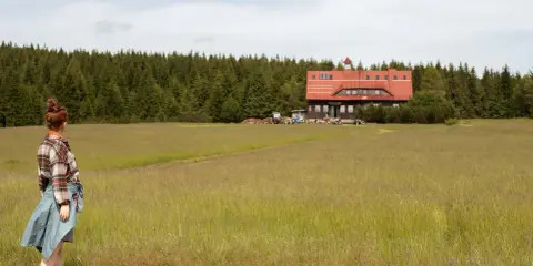 Dziewczyna w kratę podziwia schronisko na tle lasu w Górach Izerskich, Polska.