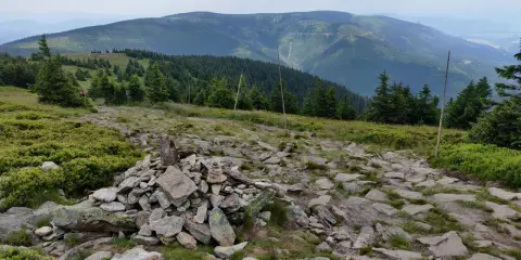 Kamienny szlak prowadzi przez zielone zbocza masywu Śnieżnika. W oddali widać kolejne pasma górskie.