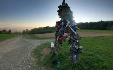 Skopiec szlak. Rzeźba z butów na rozstaju dróg, w tle zachodzące słońce i góry.