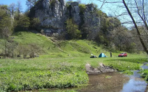 Malownicza dolina Kluczwody z rozbitymi namiotami, czerwonym samochodem i strumieniem. Skaliste zbocza porośnięte zielenią.
