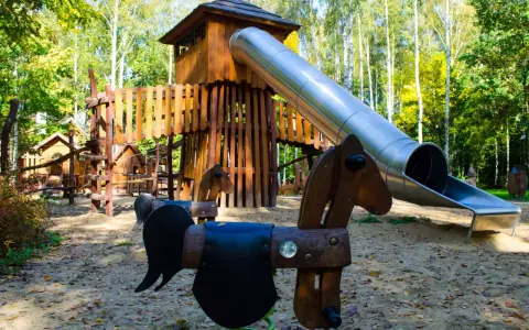 Drewniany plac zabaw z wieżą i zjeżdżalnią, idealne atrakcje dla dzieci Radom. Huśtawki w kształcie koników czekają na małych odkrywców.