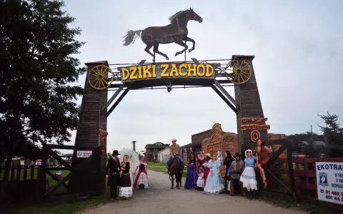 Park rozrywki Dziki Zachód koło Kołobrzegu. Grupa osób w strojach z Dzikiego Zachodu pozuje przed bramą.