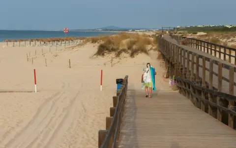 Spacer plaży z drewnianą kładką i osobą niosącą sprzęt plażowy. Grzybowo atrakcje czekają!