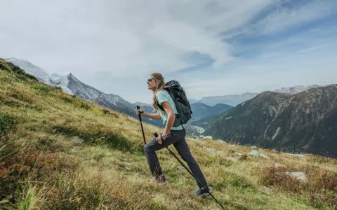 Kobieta z plecakiem i kijkami wspina się po zboczu. Widok gór i doliny. Zastanawia się, ile się idzie na Giewont.