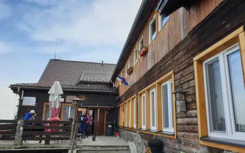 Drewniane schronisko w Górach Opawskich, z tarasem i schodami. W tle błękitne niebo z chmurami.