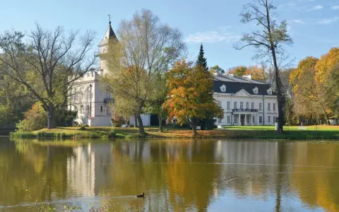Pałac w Bolimowskim Parku Krajobrazowym odbija się w spokojnej tafli jeziora, otoczony jesiennymi drzewami.