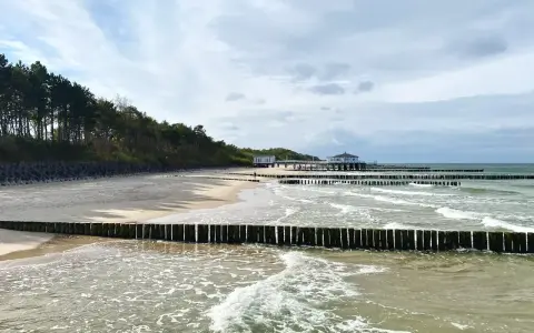 Plaża z drewnianymi falochronami i budynkami nad morzem, przypominająca najcieplejsze regiony Polski.