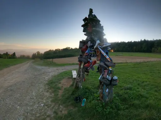 Skopiec szlak. Rzeźba z butów na rozstaju dróg, w tle zachodzące słońce i góry.