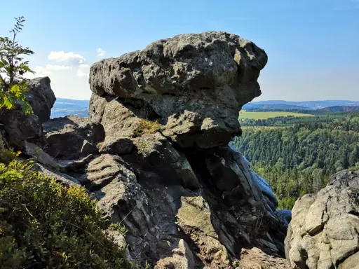 Wielkie, szare skały górują nad zieloną doliną. W oddali widać białe skały i pagórki.