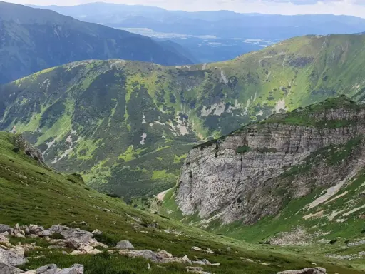 Malownicza trasa w Kościelisku. Zielone zbocza górskie, skaliste urwisko i pasma górskie w oddali tworzą zapierający dech w piersiach krajobraz.