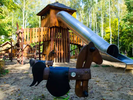 Drewniany plac zabaw z wieżą i zjeżdżalnią, idealne atrakcje dla dzieci Radom. Huśtawki w kształcie koników czekają na małych odkrywców.