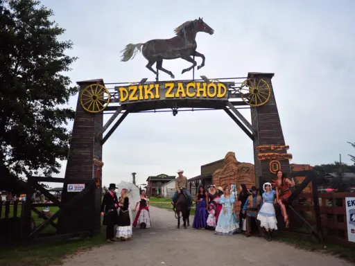 Park rozrywki Dziki Zachód koło Kołobrzegu. Grupa osób w strojach z Dzikiego Zachodu pozuje przed bramą.
