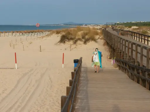 Spacer plaży z drewnianą kładką i osobą niosącą sprzęt plażowy. Grzybowo atrakcje czekają!