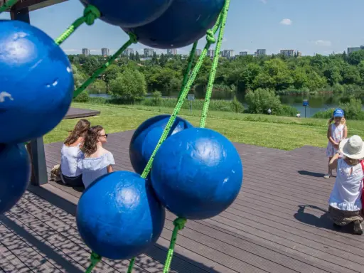 Tarnów atrakcje dla dzieci: dwie kobiety siedzą na drewnianym tarasie, a mała dziewczynka w letniej sukience i kapeluszu pozuje do zdjęcia.