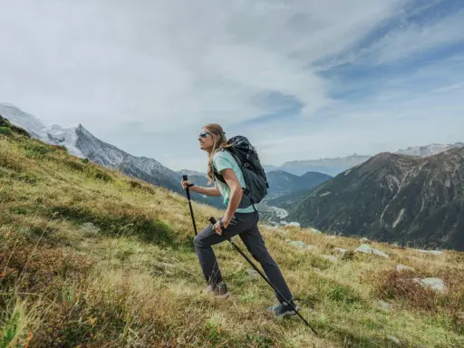 Kobieta z plecakiem i kijkami wspina się po zboczu. Widok gór i doliny. Zastanawia się, ile się idzie na Giewont.