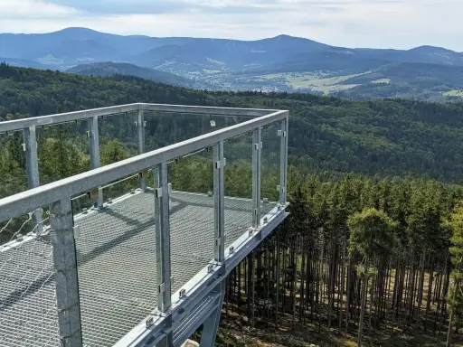 Widok z tarasu widokowego na górze Trojak w Lądku-Zdroju. Rozległe lasy i góry w tle.