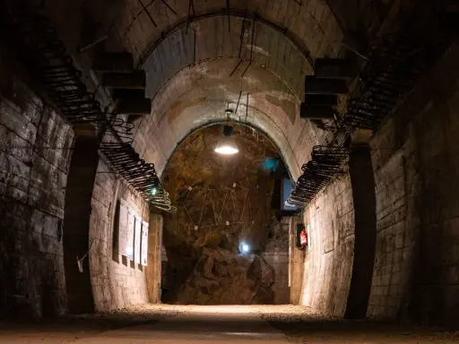 Wnętrze tunelu w Górach Sowich. Betonowe ściany, łukowe sklepienie i oświetlenie tworzą mroczny klimat.